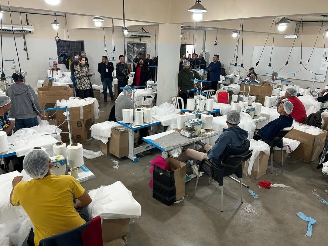 Workers in hairnets operating sewing machines in a hospital disposable gown factory