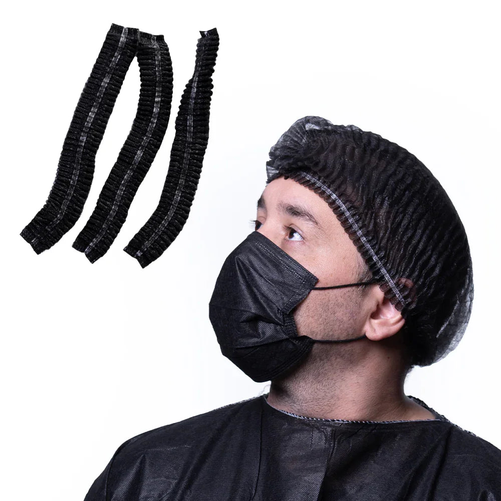 Man in black disposable bouffant cap, mask, and gown with three black bouffant caps shown