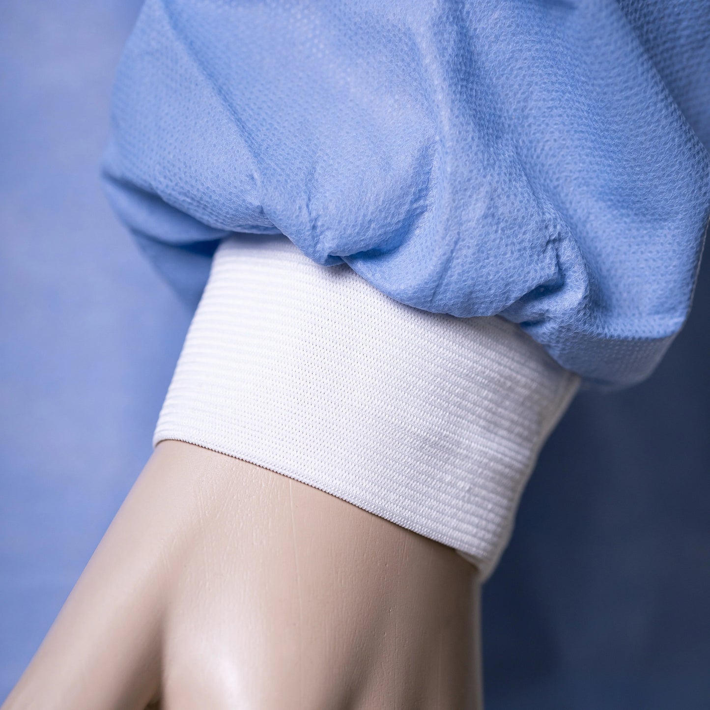 Closeup of blue disposable hospital gown sleeve with white cuff on mannequin hand
