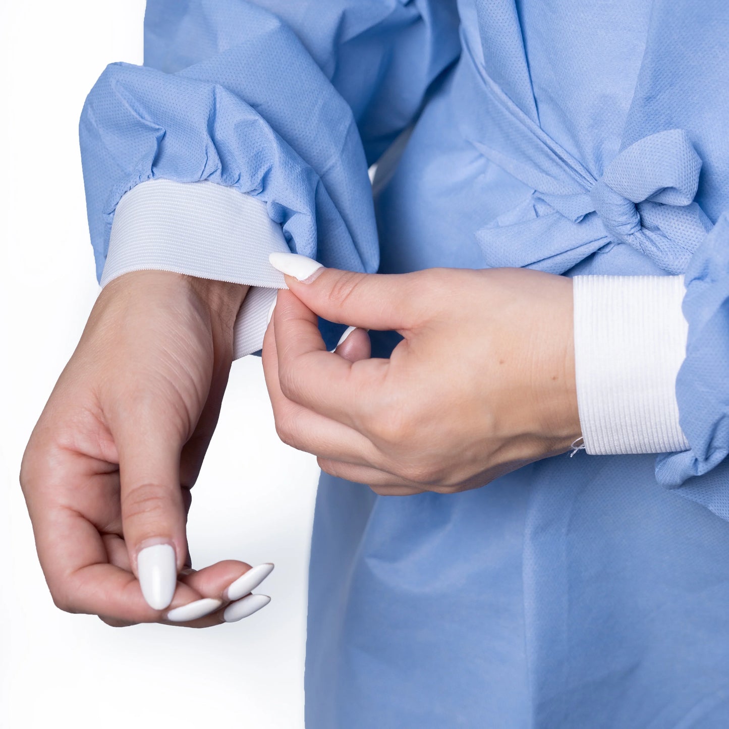 Close-up of hands adjusting blue disposable hospital gown with white knit cuffs, MEGA USA